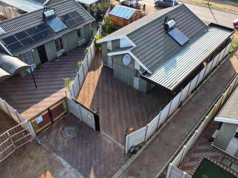 Aerial view of a residential property featuring a paved driveway, solar energy installations, and secure perimeter walling.