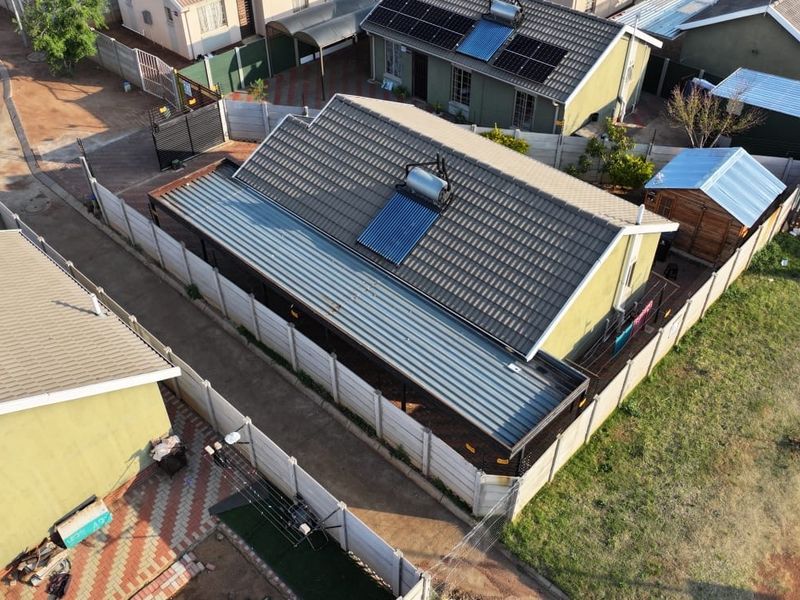 Aerial view of the property showing the main house with a tiled roof, solar water heating system, and enclosed perimeter walling.