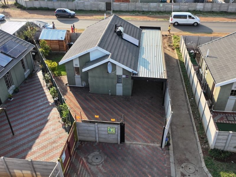 Aerial view of a residential property featuring a tiled roof with solar water heating, a paved driveway, and secure perimeter walling.