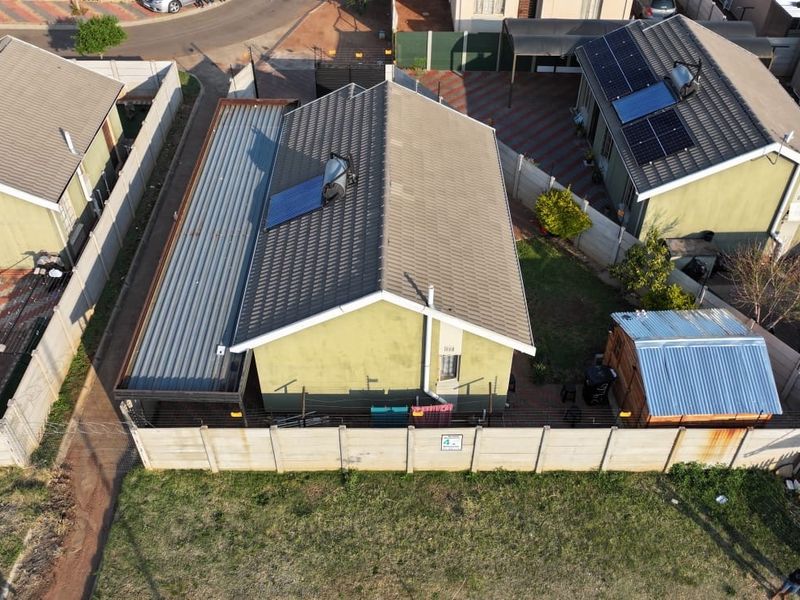 Aerial view of a residential property featuring a tiled roof with solar water heating, a corrugated metal extension, and a secure precast boundary wall.