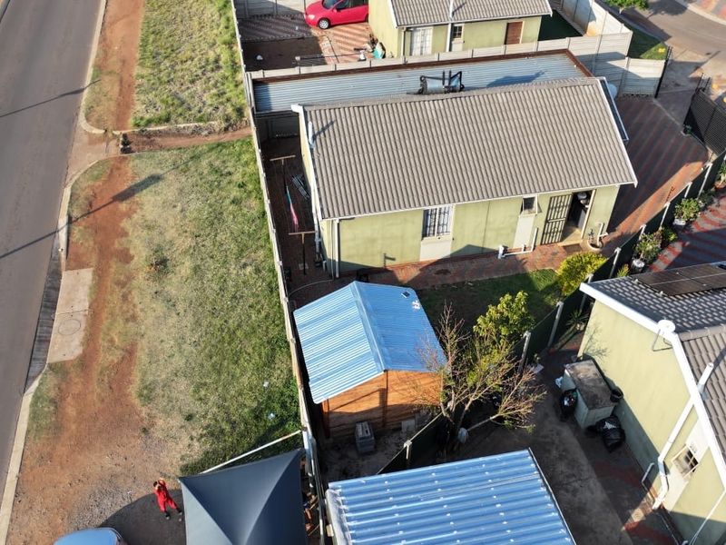 Aerial view of the property showing the main dwelling, corrugated metal roofing, perimeter fencing, and outdoor storage shed.