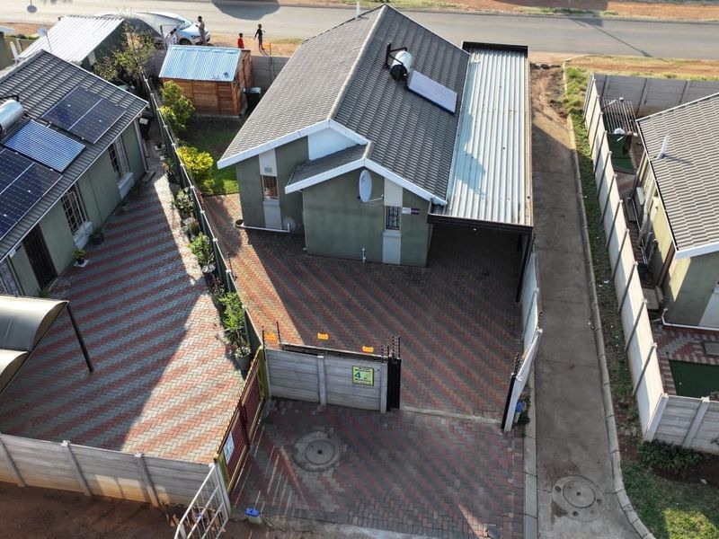 Aerial view of a residential property featuring a paved driveway, carport, solar geyser, and solar panels, enclosed by precast concrete boundary walls.