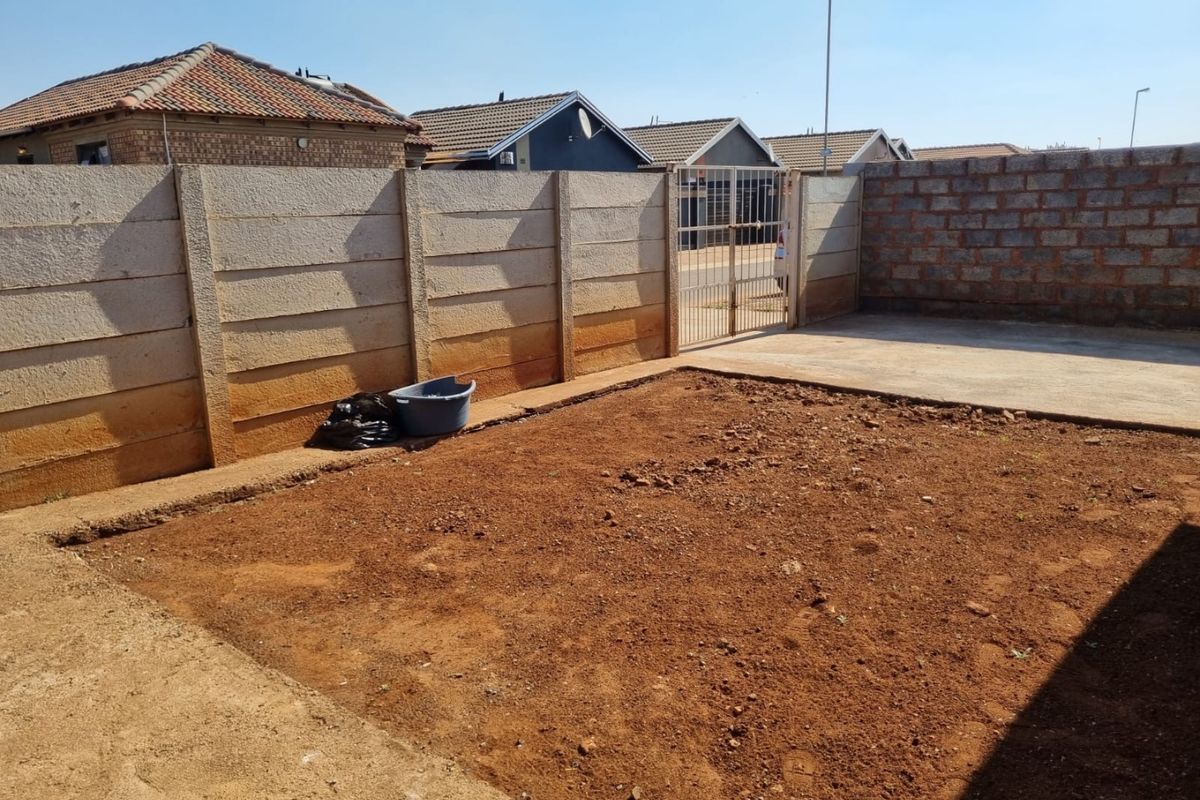 Rear yard area featuring a precast concrete boundary wall, concrete paving, and an unlandscaped soil garden space ready for development.