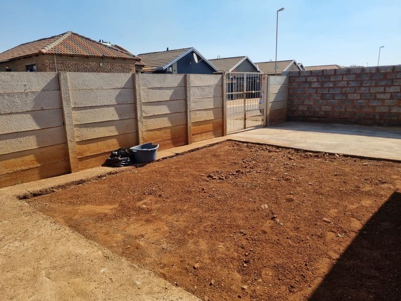 Rear yard area featuring a precast concrete boundary wall, concrete paving, and an unlandscaped soil garden space ready for development.