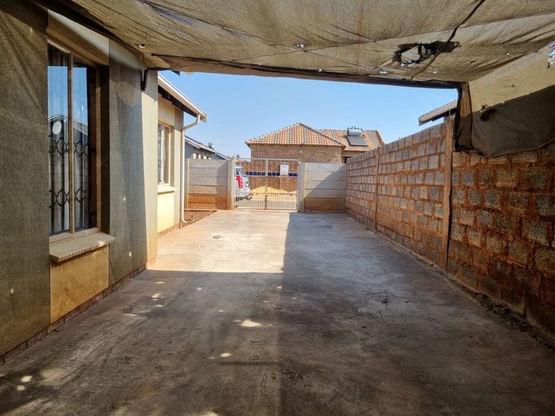A paved rear exterior area featuring a concrete boundary wall, metal security gate, and a damaged shade cloth canopy structure.