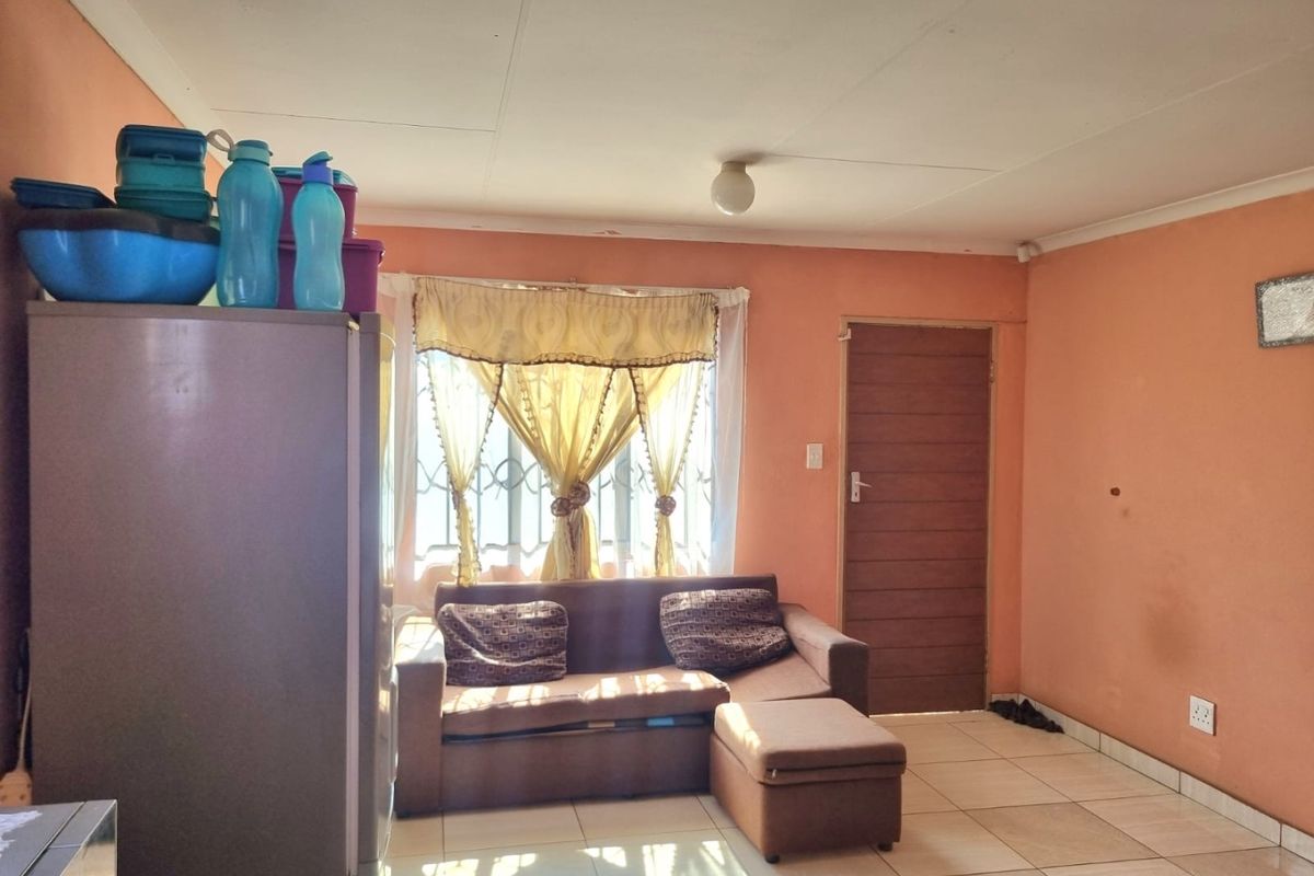 A living room area featuring tiled flooring, a window with security bars, and a standard door, providing a functional base for interior updates.