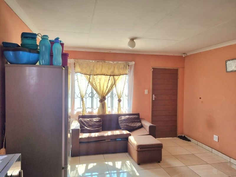 A living room area featuring tiled flooring, a window with security bars, and a standard door, providing a functional base for interior updates.