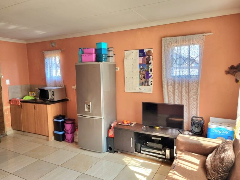 Open-plan living area featuring tiled flooring and a compact kitchen corner with built-in cabinetry and laminate countertops.