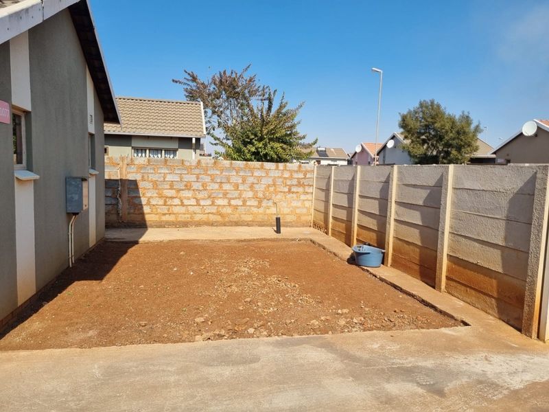 A rear exterior view of the property featuring a concrete apron and an unlandscaped yard enclosed by precast and brick boundary walls.