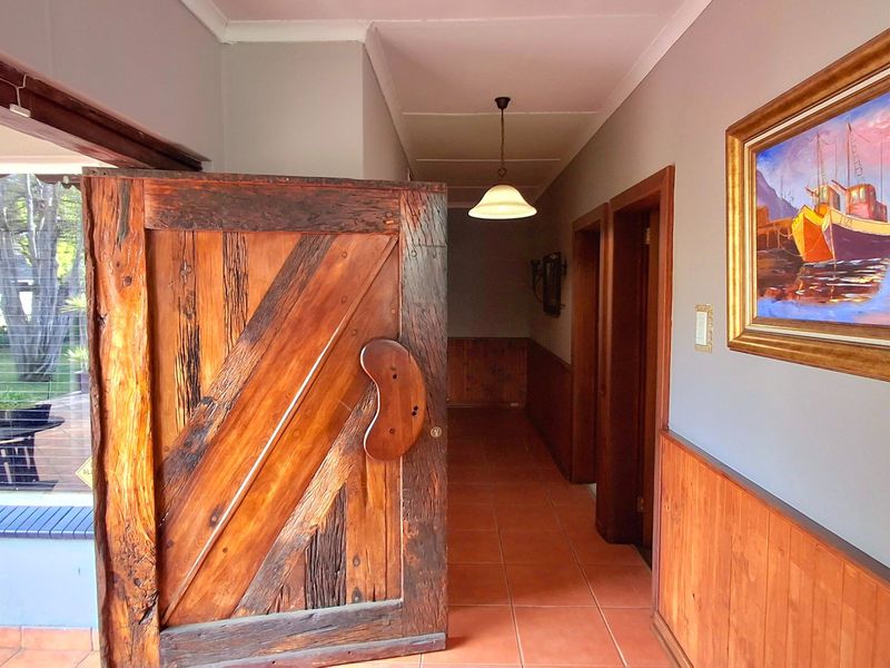 A welcoming hallway featuring warm terracotta floor tiles, classic timber wainscoting, and a distinctive solid wood door leading to the living area.