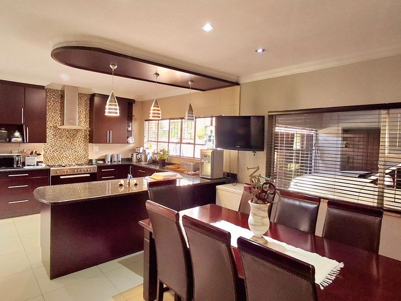 Spacious open-plan kitchen and dining area featuring dark wood cabinetry, granite countertops, modern lighting, and tiled flooring, creating a functional and cohesive living space.