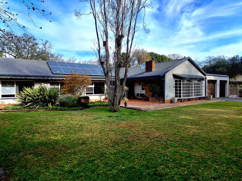A spacious rear exterior view of the house featuring a large lawn, paved patio area, and roof-mounted solar panels.