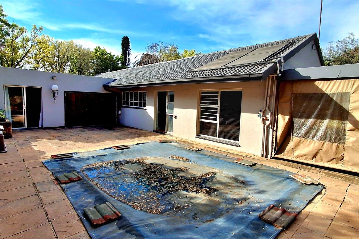Rear exterior view featuring a paved patio area, swimming pool with cover, and solar water heating panels on the roof.