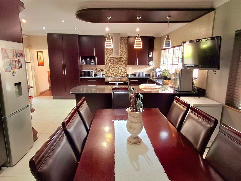 Spacious open-plan kitchen and dining area featuring dark wood cabinetry, granite countertops, mosaic backsplash, and modern recessed and pendant lighting.