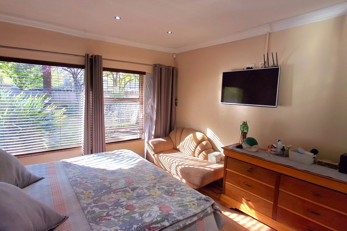 A well-lit bedroom featuring large windows with blinds, recessed ceiling lighting, and a wall-mounted television.