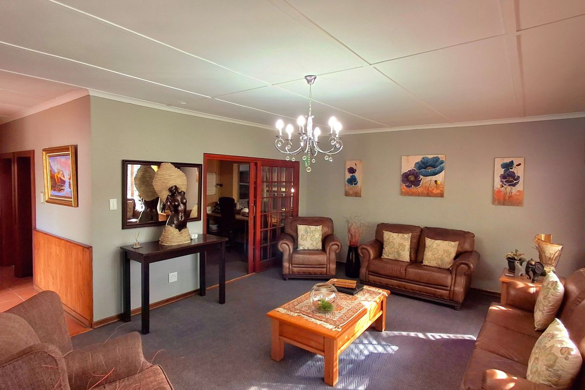 A spacious living room featuring carpeted flooring, a central chandelier, and glass-paneled french doors leading to an adjacent room.