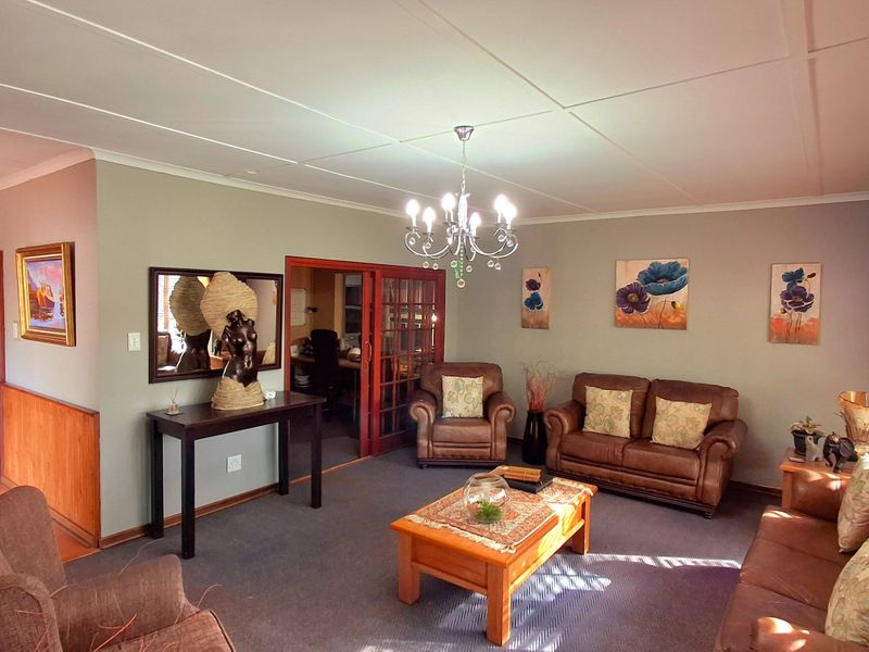 A spacious living room featuring carpeted flooring, a central chandelier, and glass-paneled french doors leading to an adjacent room.