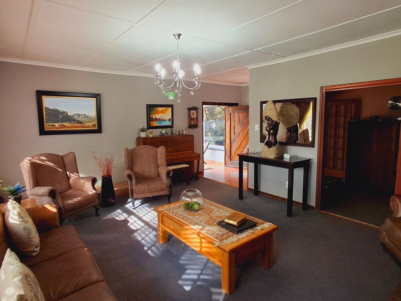 A spacious living room featuring carpeted flooring, a central chandelier, and a sliding wooden door leading to an adjacent tiled entryway.