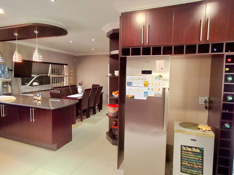 Open-plan kitchen and dining area featuring dark wood cabinetry, a granite-topped island, integrated wine storage, and recessed lighting throughout the space.