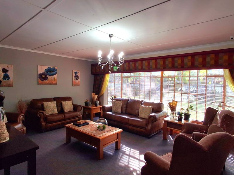 A spacious living room featuring a large window with blinds, a central chandelier, and a tiled ceiling finish.