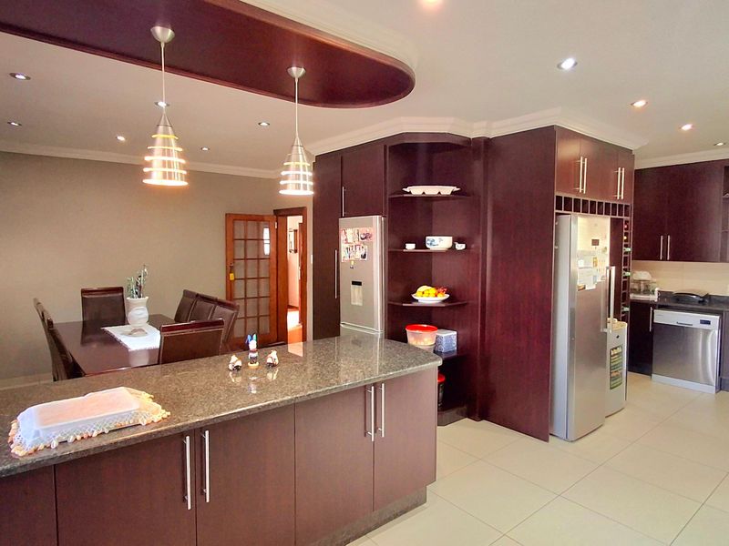 Spacious open-plan kitchen and dining area featuring dark wood cabinetry, granite countertops, modern pendant lighting, and neutral tiled flooring throughout.