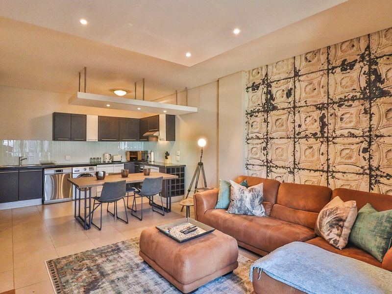 Modern open-plan living area featuring a well-equipped kitchen with dark cabinetry, integrated wine storage, and recessed lighting, seamlessly flowing into the lounge space.