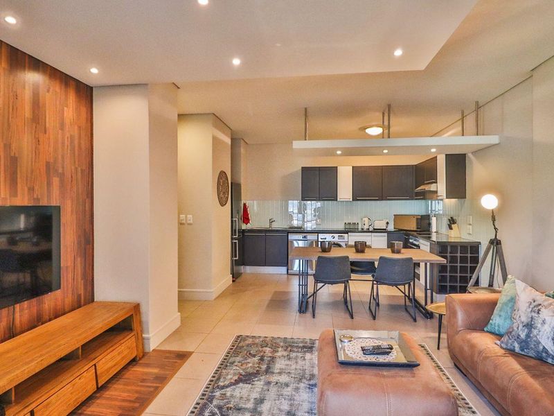 Modern open-plan living area featuring a wood-paneled feature wall, recessed lighting, and a contemporary kitchen with sleek cabinetry and tiled flooring.