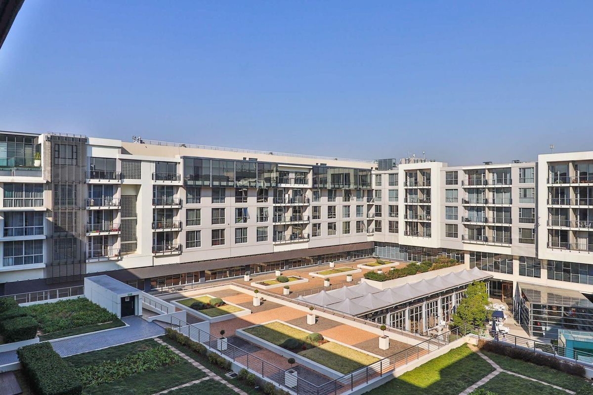An elevated view of a modern apartment complex featuring a central landscaped courtyard, paved walkways, and multiple levels of private balconies.