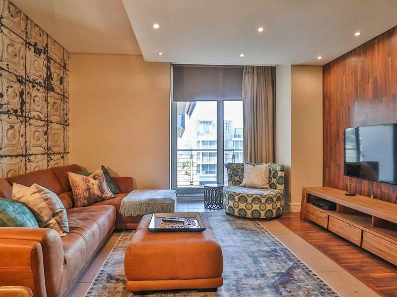 A well-appointed living room featuring a wood panel feature wall, recessed ceiling lighting, and access to a private balcony through sliding glass doors.