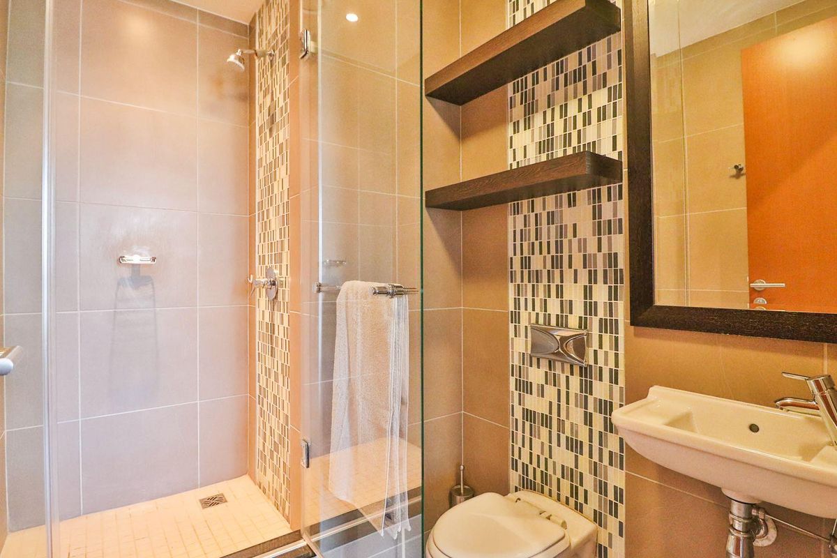 Modern bathroom featuring a glass-enclosed shower, mosaic tile accents, wall-hung toilet, and a sleek wall-mounted basin with floating shelving.