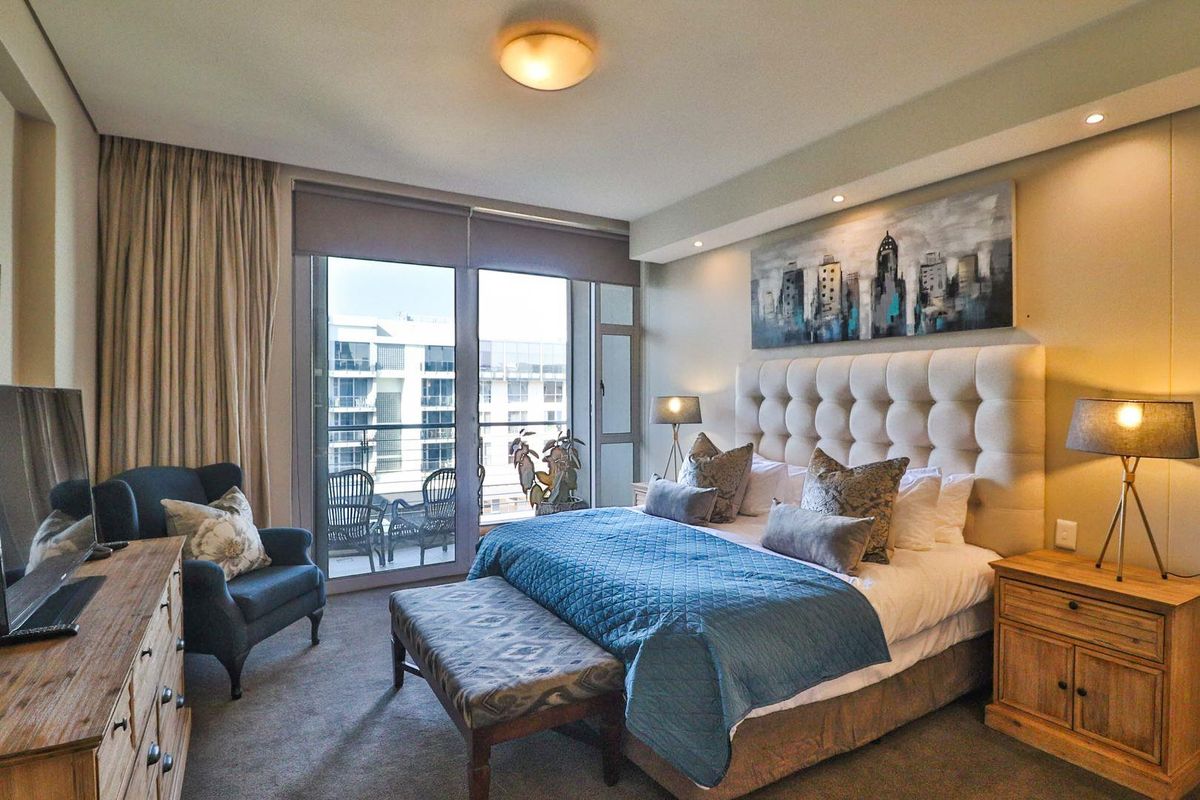 A well-appointed bedroom featuring carpeted flooring, recessed lighting, and a large sliding glass door providing access to a private balcony.