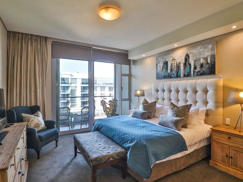 A well-appointed bedroom featuring carpeted flooring, recessed lighting, and a large sliding glass door providing access to a private balcony.