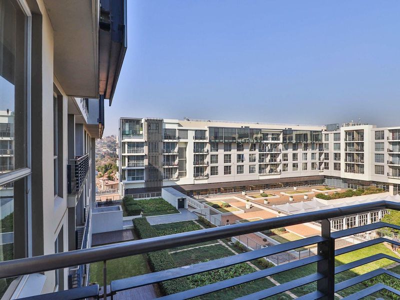 A view from a balcony overlooking a modern apartment complex courtyard with landscaped gardens and paved walkways.