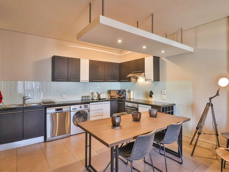 Modern open-plan kitchen featuring dark and white cabinetry, integrated appliances, tiled backsplash, and a distinctive suspended ceiling feature with recessed lighting.