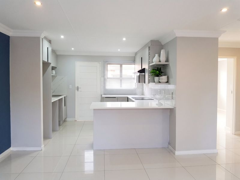 Modern kitchen featuring sleek built-in cabinetry, stone countertops, a breakfast bar, and integrated hob with extractor fan, finished with polished floor tiles.