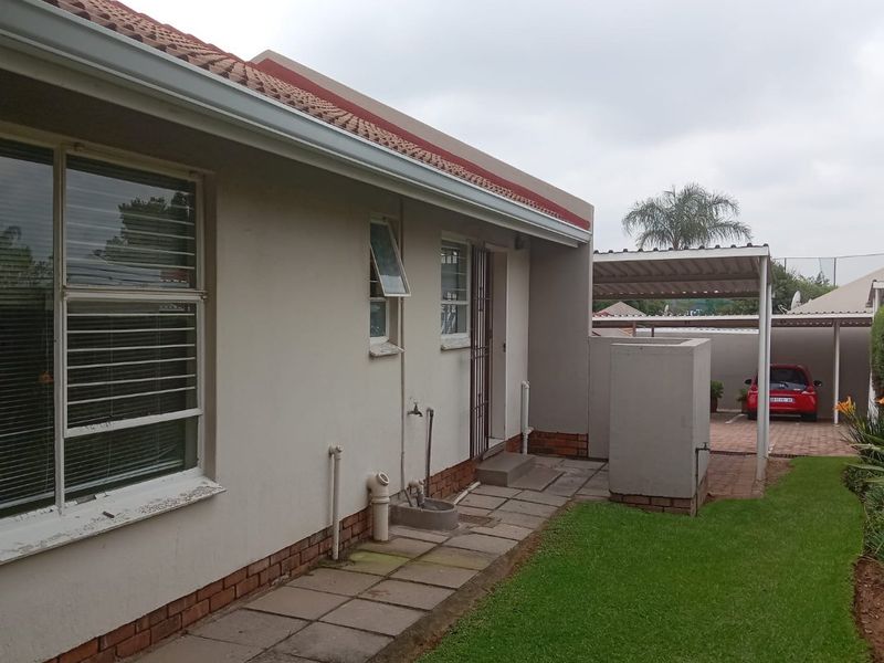 Rear exterior view of the apartment featuring a paved walkway, external water tap, and a covered carport area with a small lawn.