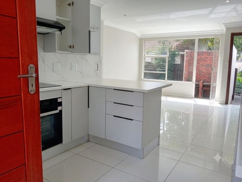 Modern open-plan kitchen featuring sleek cabinetry, marble-look splashback, and integrated appliances, flowing seamlessly into a bright living area with large glass doors.