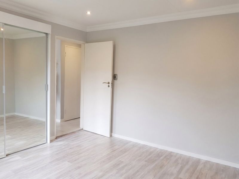 A bright, empty bedroom featuring light-toned laminate flooring, recessed downlighting, and a large built-in mirrored wardrobe.