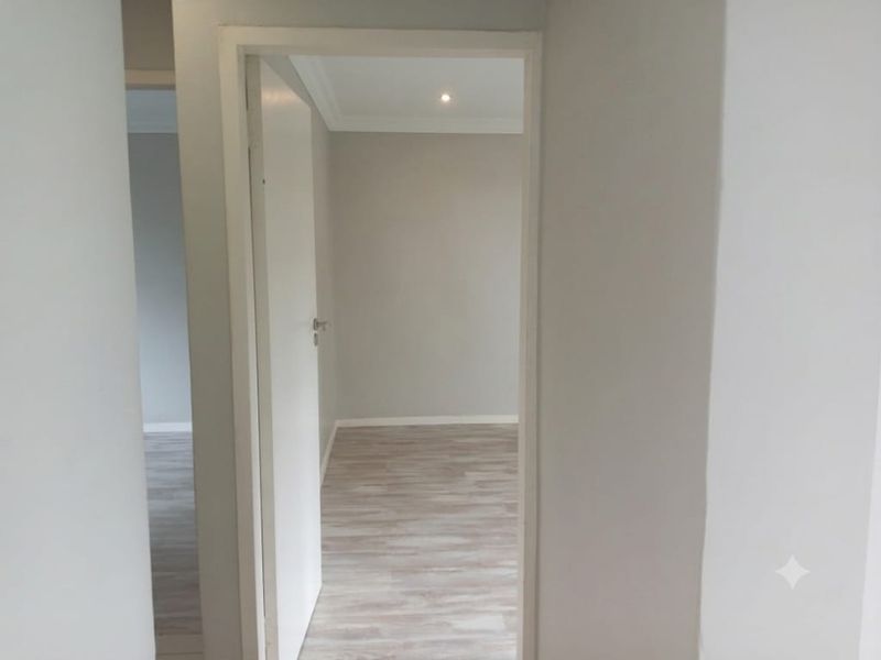 A bright, empty hallway featuring light-toned laminate flooring and neutral walls, providing a clean and modern transition between rooms.