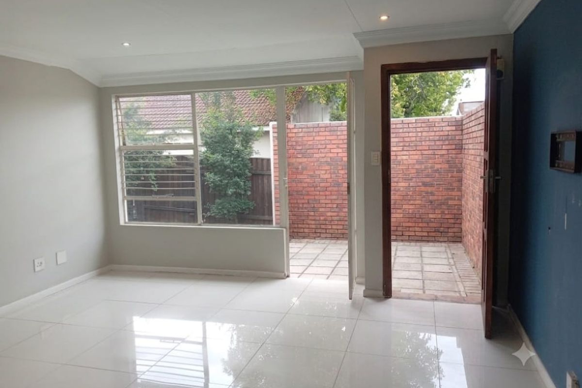 Bright, empty living area featuring polished tiled floors, recessed lighting, and direct access to a private paved patio through a glass door.