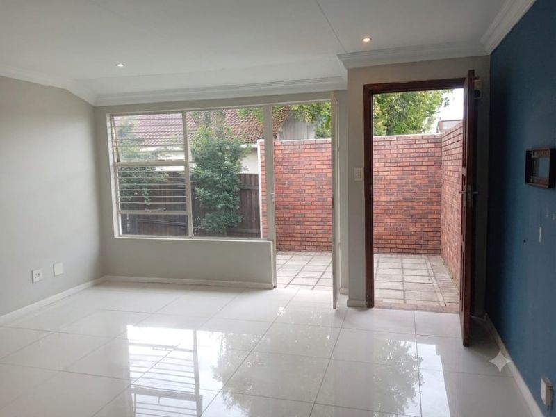 Bright, empty living area featuring polished tiled floors, recessed lighting, and direct access to a private paved patio through a glass door.