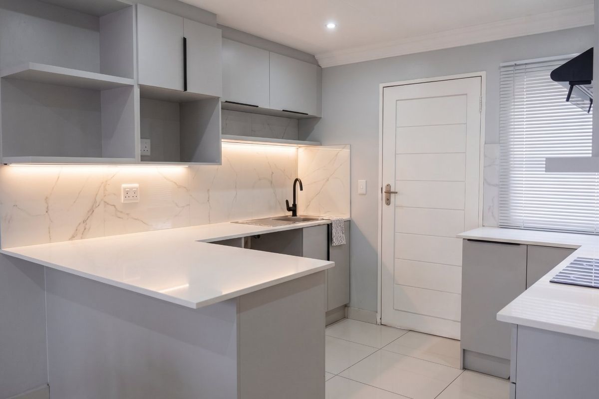 Modern kitchen featuring sleek grey cabinetry, white quartz countertops, marble-look backsplash, and integrated under-cabinet lighting in a clean, contemporary finish.