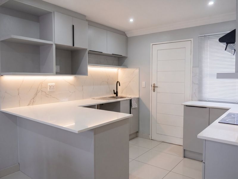 Modern kitchen featuring sleek grey cabinetry, white quartz countertops, marble-look backsplash, and integrated under-cabinet lighting in a clean, contemporary finish.