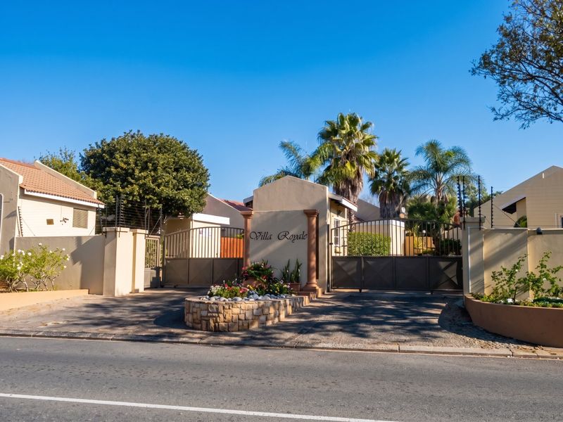 The secure gated entrance to Villa Royale apartment complex, featuring a stone masonry planter, perimeter walls, and electric fencing.