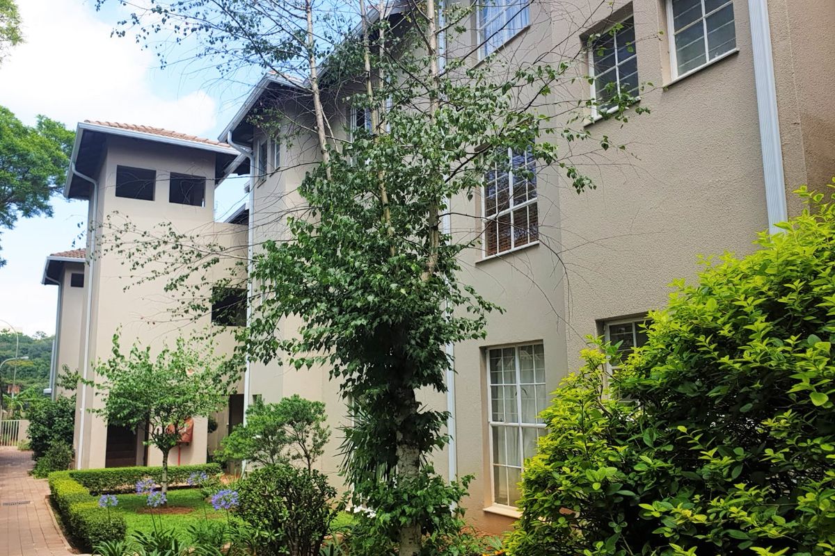 A view of the apartment building exterior featuring a well-maintained facade, sash windows, and a landscaped garden area with a paved walkway.