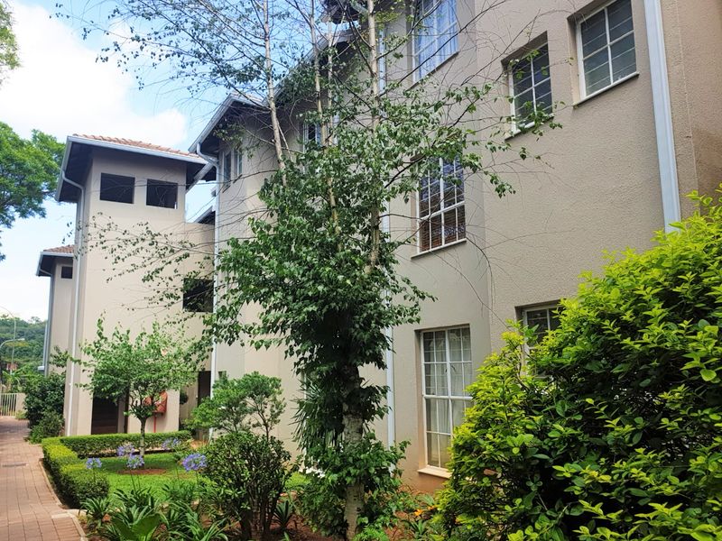 A view of the apartment building exterior featuring a well-maintained facade, sash windows, and a landscaped garden area with a paved walkway.