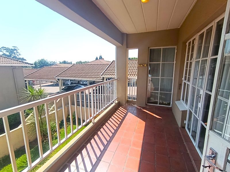 A covered balcony featuring tiled flooring and a metal balustrade, offering an outdoor space accessible through glass panel doors.