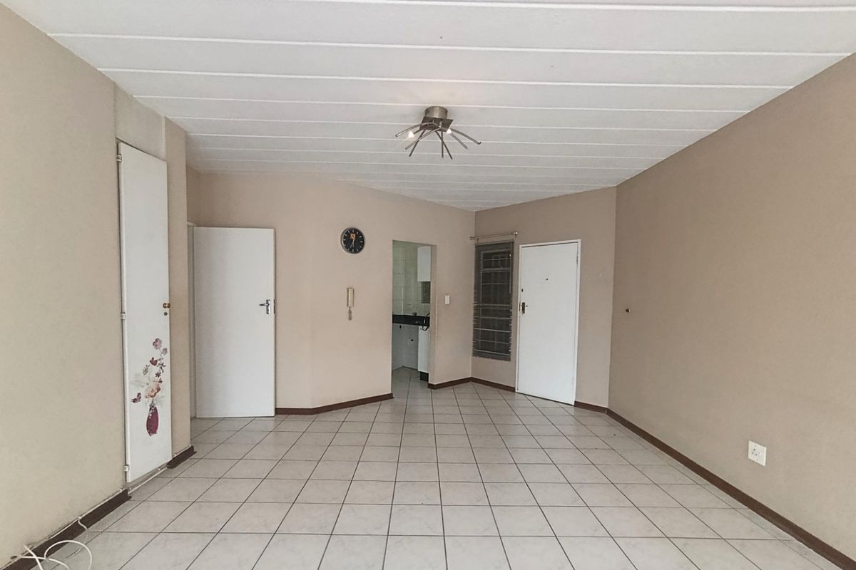 An empty, neutrally painted living area featuring tiled flooring, a central ceiling light, and access to adjacent rooms.