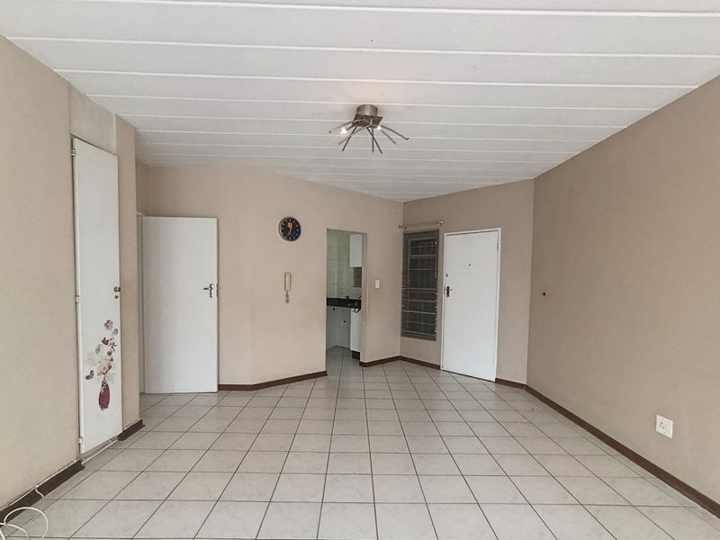 An empty, neutrally painted living area featuring tiled flooring, a central ceiling light, and access to adjacent rooms.