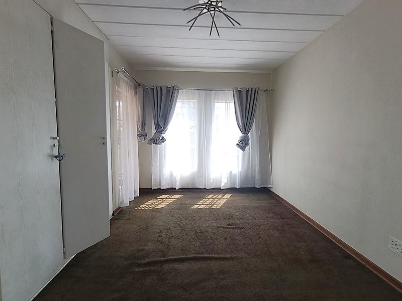 An empty bedroom featuring built-in cupboards, carpeted flooring, and a window with natural light, offering a blank canvas for renovation.
